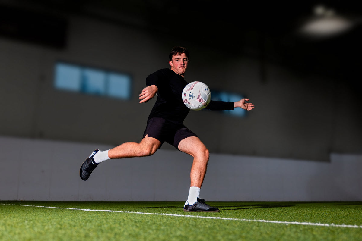 Player volleying a soccer ball indoors wearing Dominari Indoor shoes