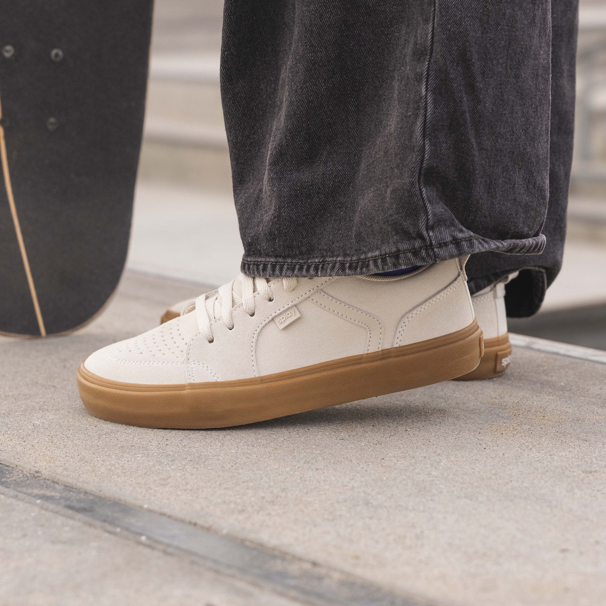 A close-up of a person wearing baggy black jeans and REV low top sneakers from Splay. 