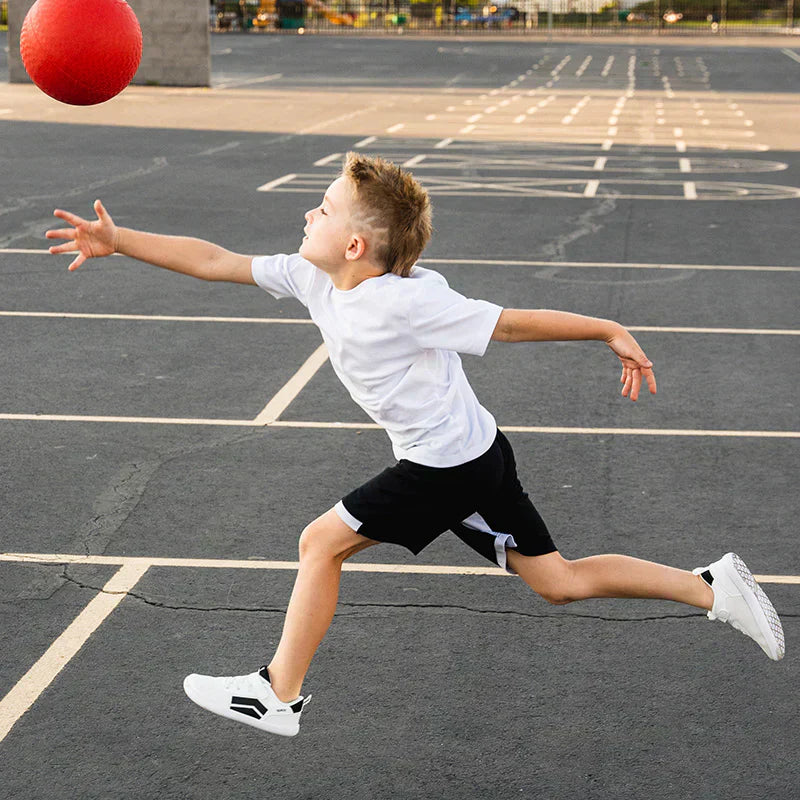 A small boy is trying to catch a red ball while wearing the DASH Spark White from Splay’s kids’ collection. 