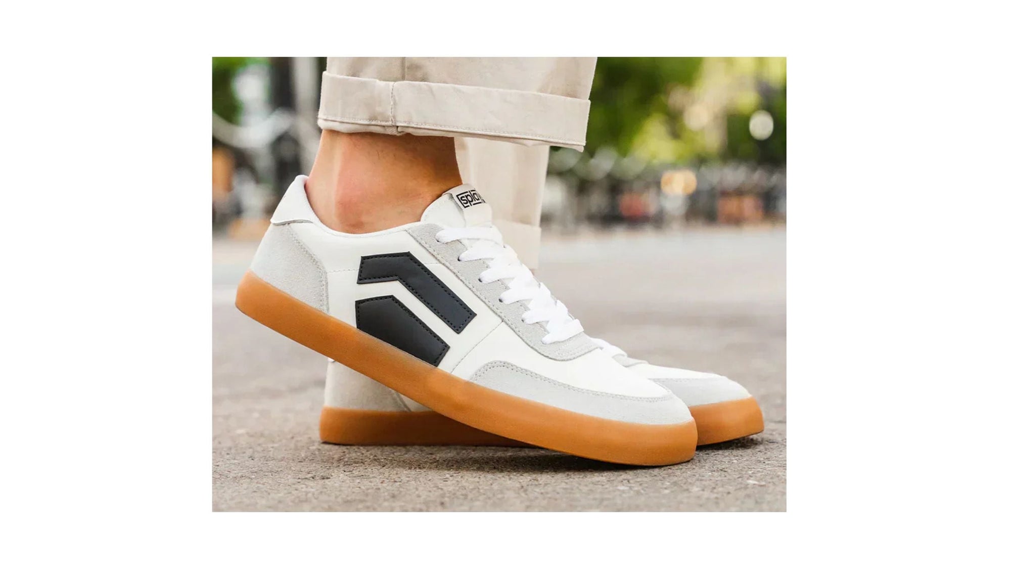 White and gray lace-up minimalist sneakers with black side accents and gum soles, standing on a street in rolled-up beige pants.