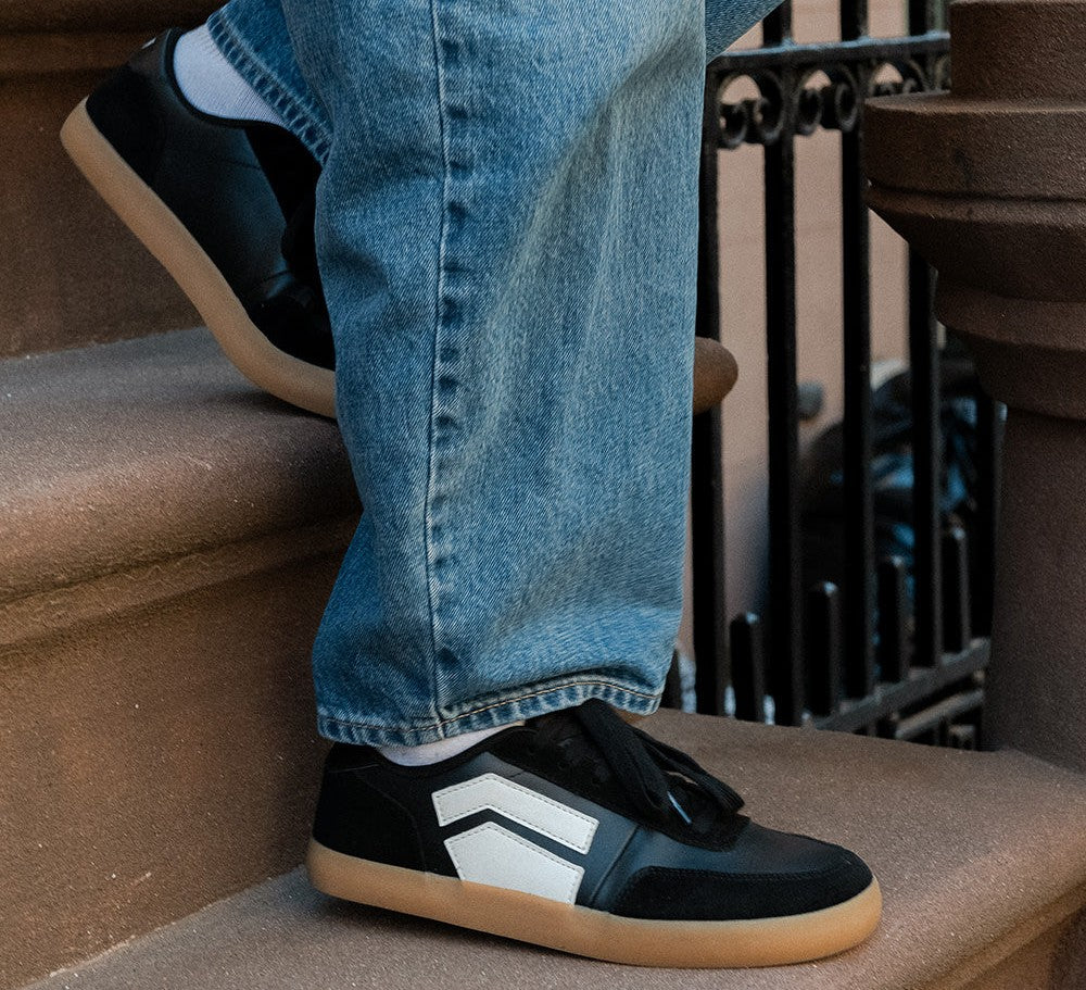 Person walking up brownstone steps wearing black and white Splay barefoot sneakers with gum soles and blue jeans.
