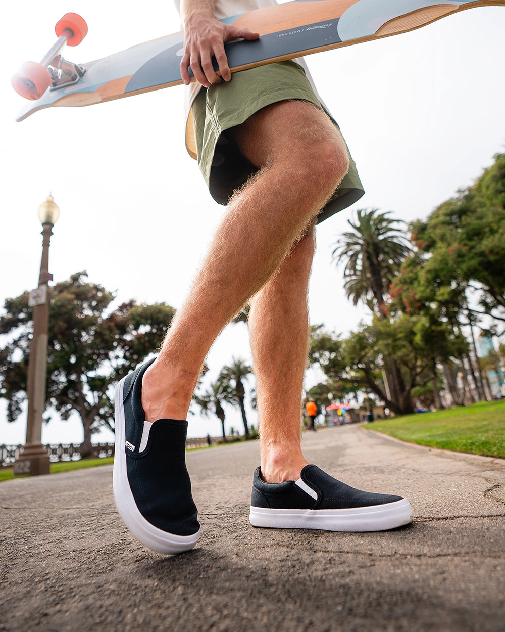 Skater walking in Splay REV SO Berlin barefoot shoes while carrying a longboard