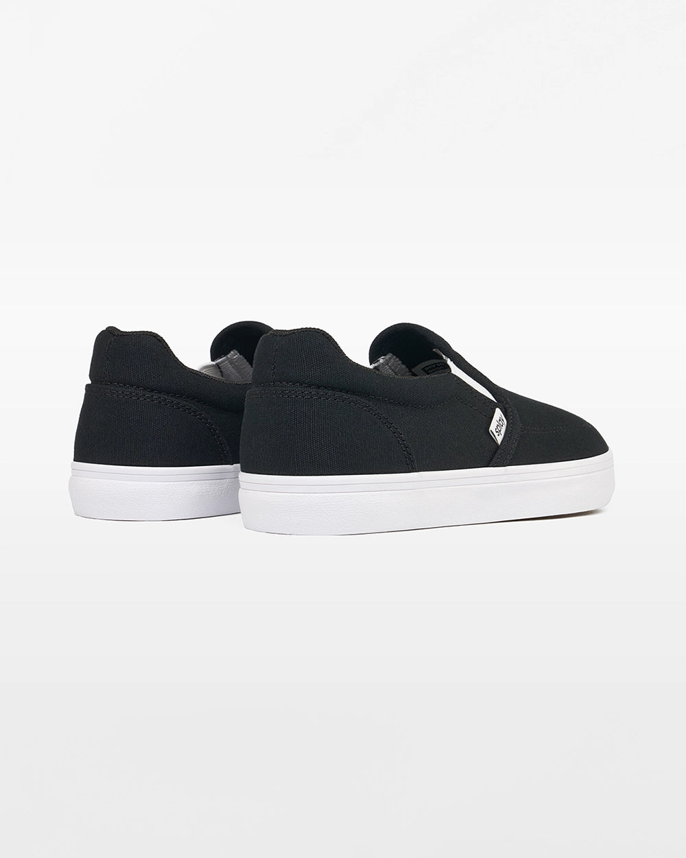 Rear angled view of a pair of black Splay Kids REV SO Berlin canvas barefoot slip-on shoes with white soles.