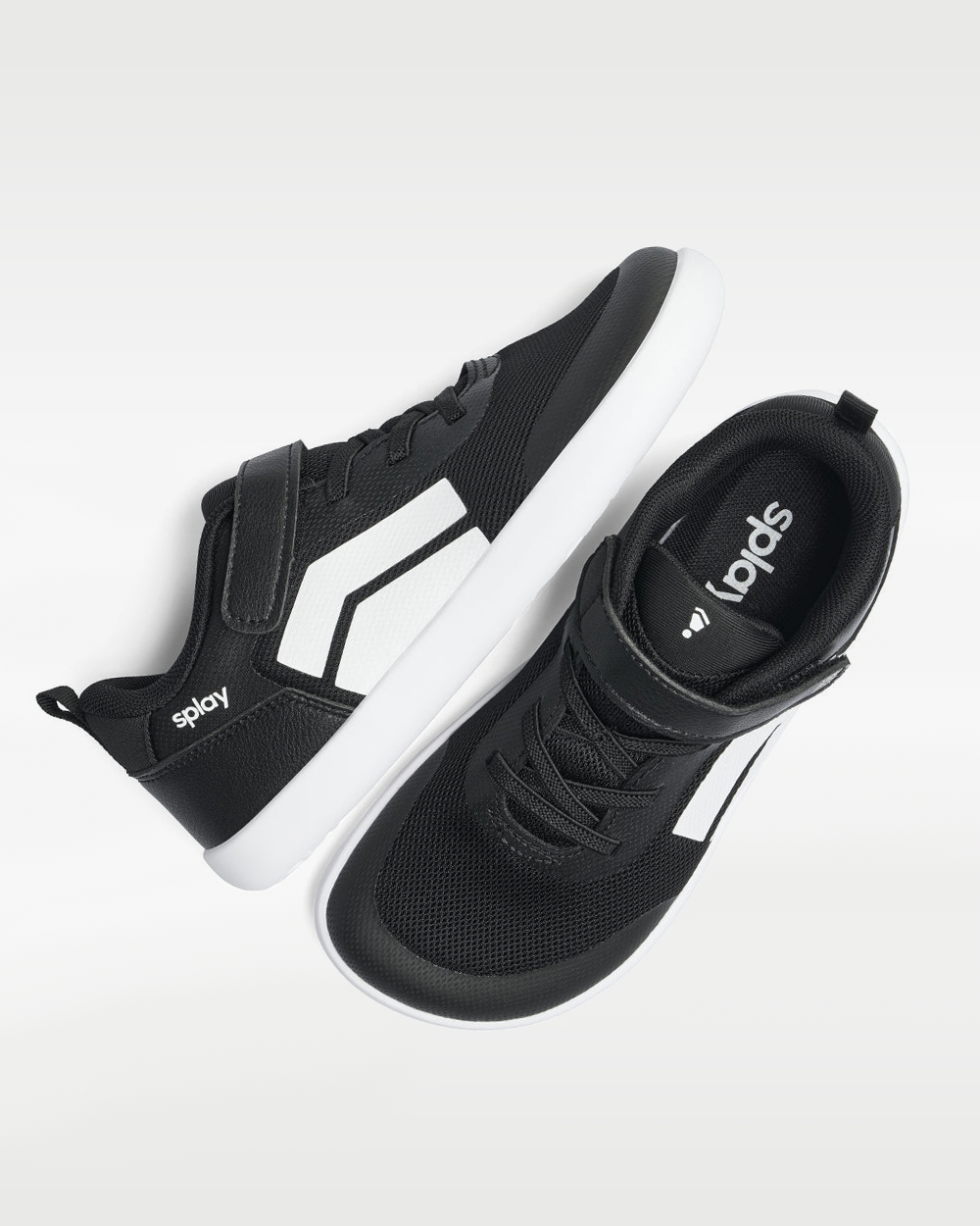Splay Dash Kids Core Black barefoot shoes — kids' low-top sneaker with a strap and laces, pair shot from above, one shoe tipped up to show the insole