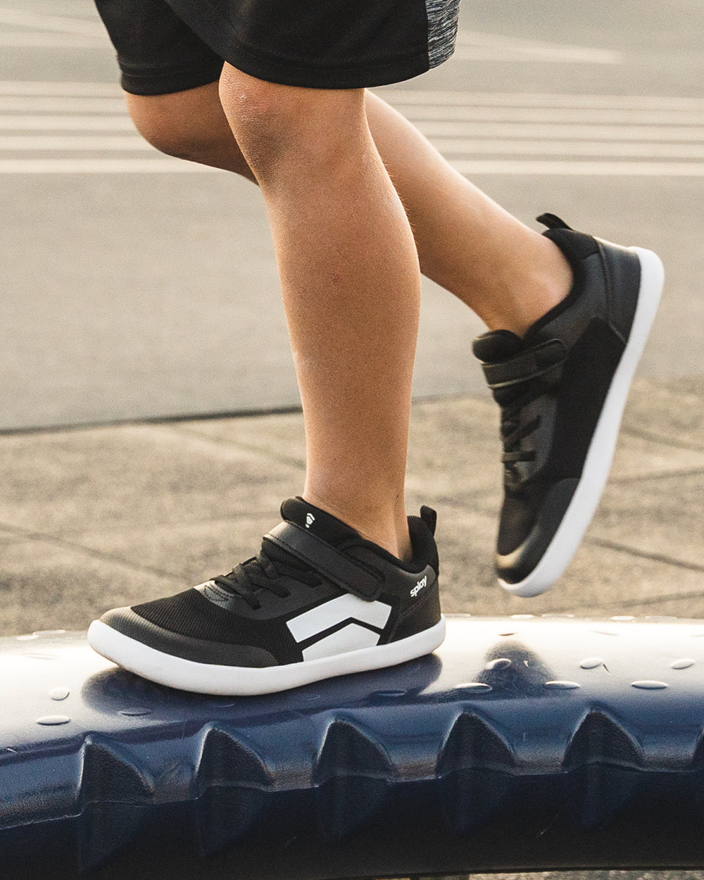 Splay Dash Kids Core Black barefoot shoes — kids' low-top sneaker with a strap and laces, lifestyle photo, the shoes shown in use outdoors