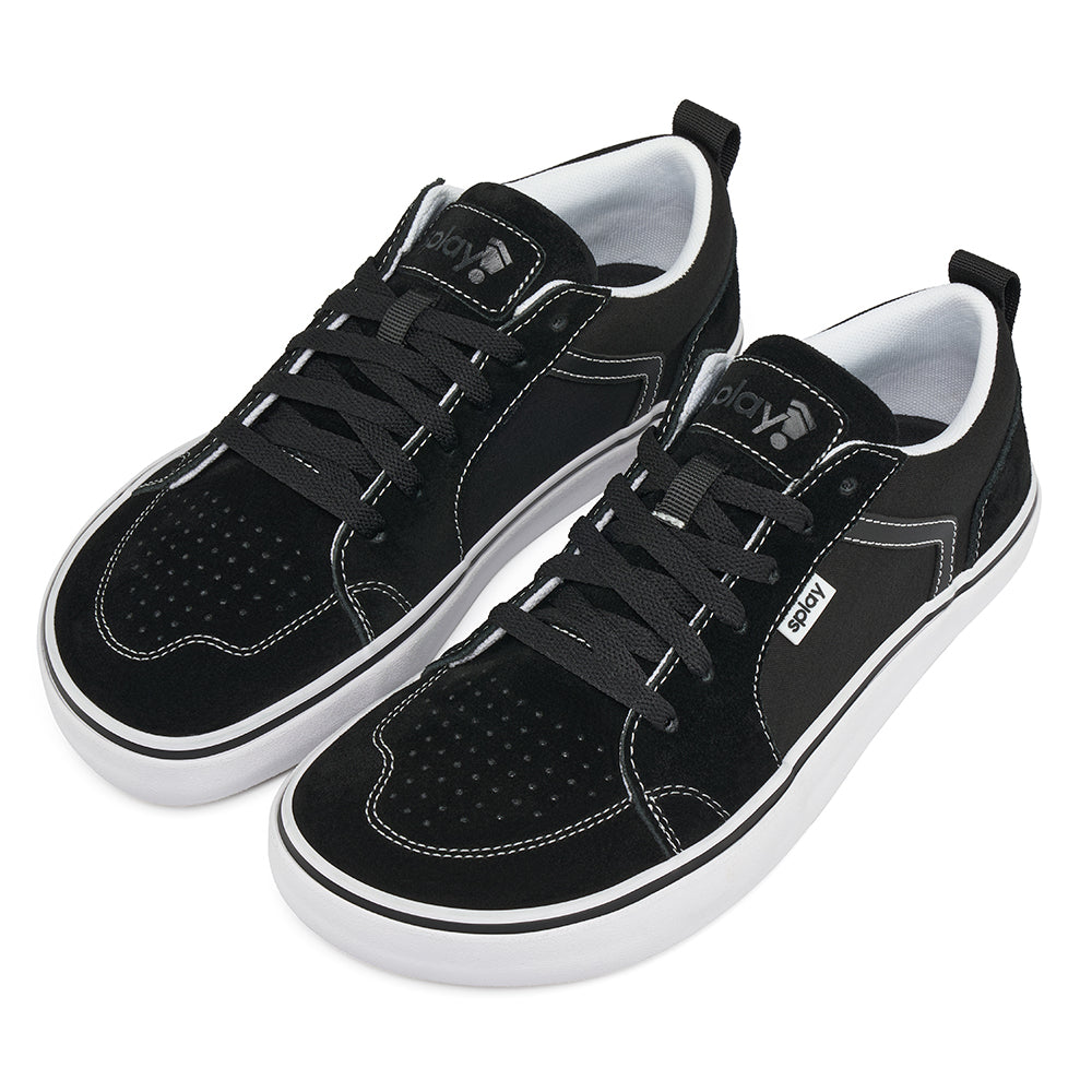 On a white background, the high side angle of a pair of black REV LTS Los Angeles sneakers showing off the white foxing with a black stripe over it. Black canvas upper with black laces. 